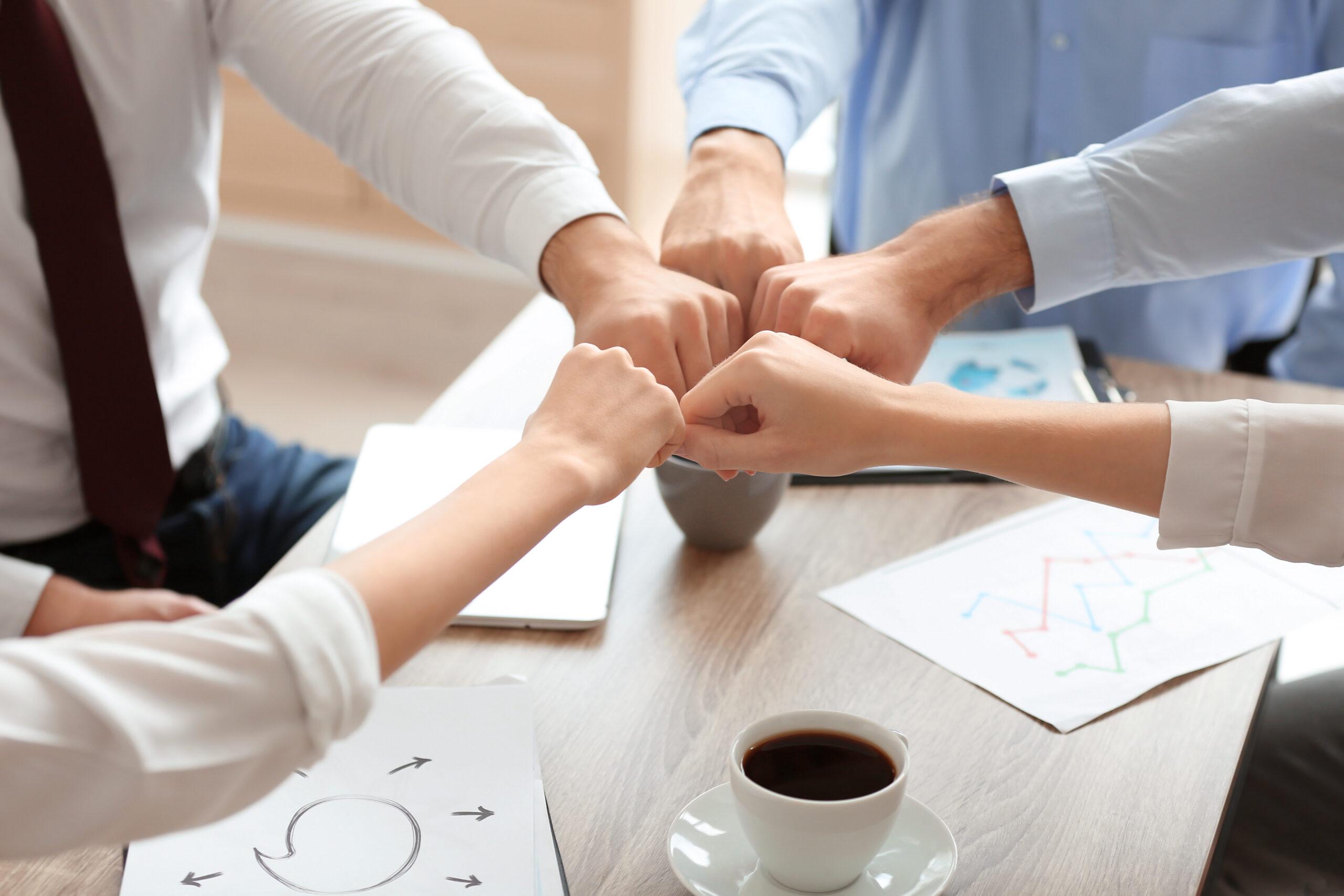 Young people in office wear putting hands together indoors